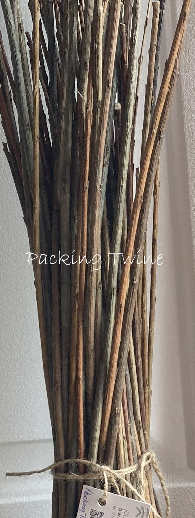 Bunch of twigs tied together with a tag on a plain background, branded Packing Twine